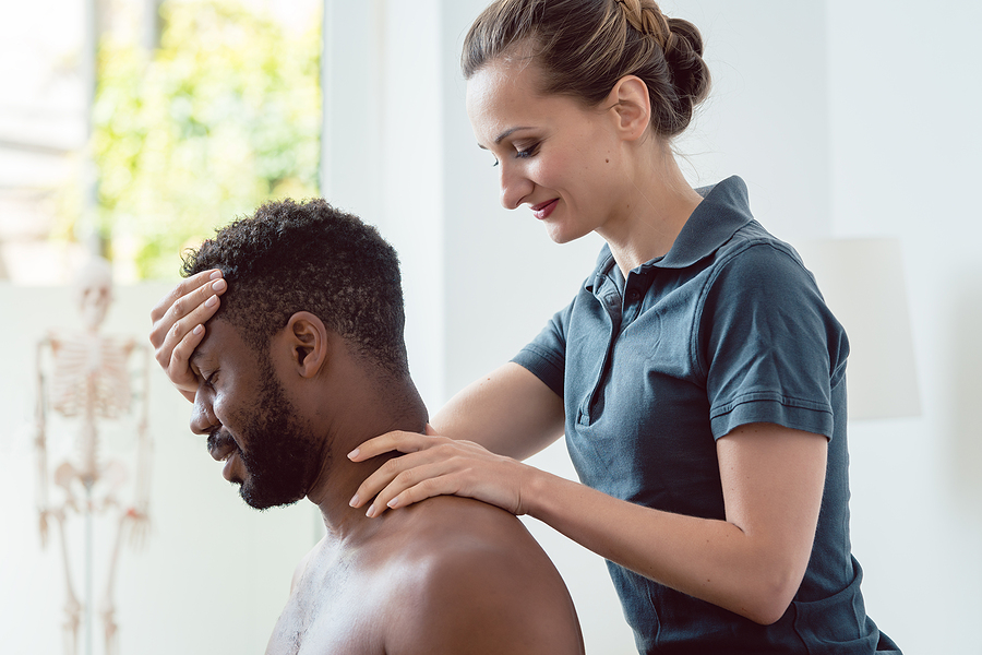 Woman physical therapist massaging young black man holding his head